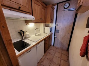 Una cucina compatta con mobili in legno, un lavandino bianco, un forno a microonde e una sveglia appesa al muro.