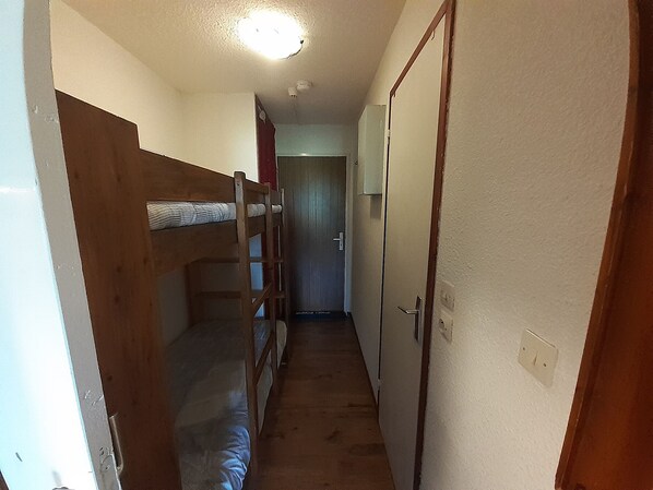 A narrow hallway with bunk beds on one side and a door on the other. - Cozy studio in Valfréjus, near the slopes (Valfréjus)