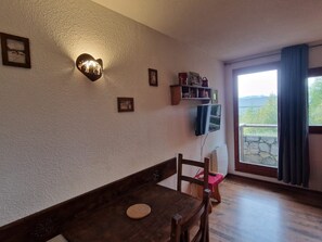 A room with a wooden table, a chair, a heart-shaped light fixture, a mounted television, and a stone wall. - Cozy studio in Valfréjus, near the slopes (Valfréjus)
