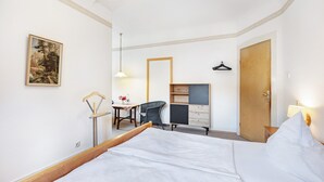 Une chambre d’hôtel avec un lit, un bureau, une chaise, une armoire et un tableau au mur.