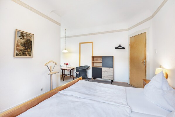 Une chambre d’hôtel avec un lit, un bureau, une chaise, une armoire et un tableau au mur.