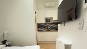 Ein Hotelzimmer mit einem Bett, einem an der Wand montierten Fernseher, einer Küchenzeile inklusive Mikrowelle und einem kleinen Tisch mit einer Pflanze.