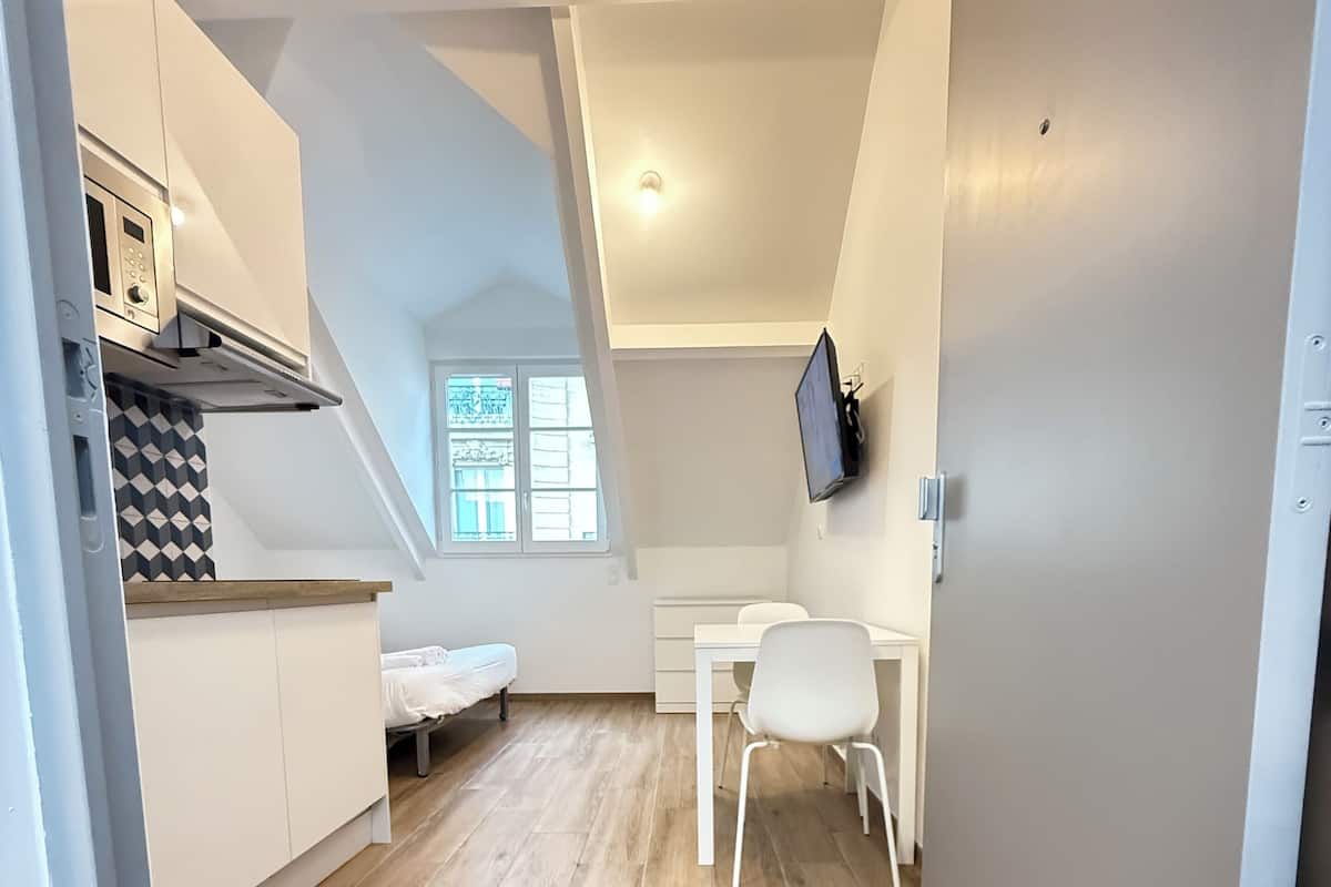 A compact kitchen with a microwave, a small dining table, and a white chair.