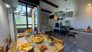 A dining area with a wooden table set for breakfast, a TV, and a kitchen area with a fridge and microwave. - Apartment at the foot of the slopes in Vars Les Claux, pets allowed (Vars)