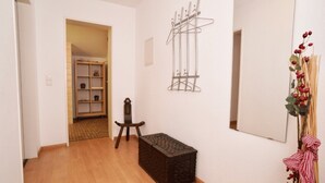 A hallway with a wooden floor, a small wooden chest, a metal coat rack, a mirror, and a shelf with items. - Apartment '2' with Shared Terrace, Balcony and Wi-Fi (Weil am Rhein)