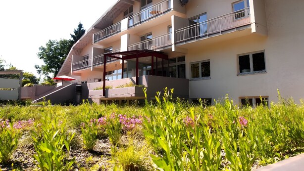 A multi-story building with balconies, a covered outdoor area, and a garden with various plants. - Apartment '1' with Shared Terrace, Balcony and Wi-Fi (Weil am Rhein)