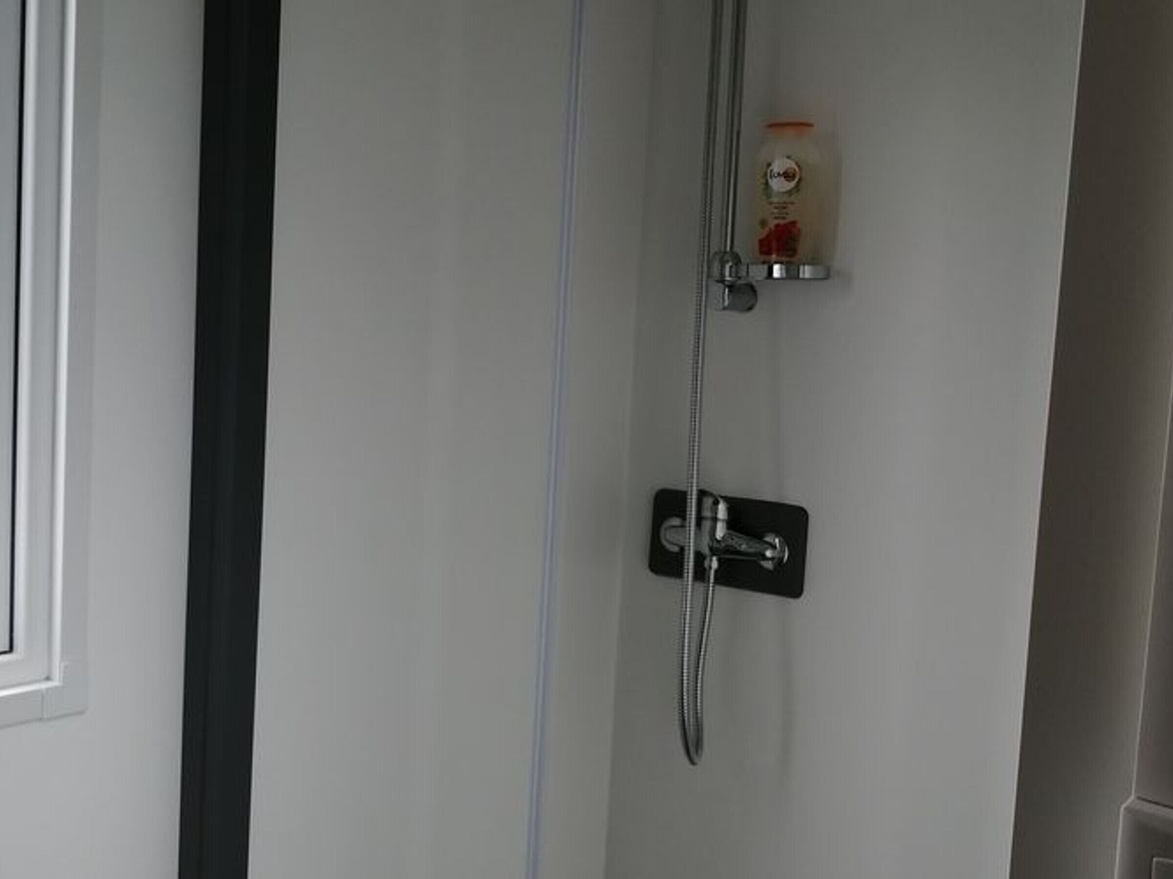 A shower with a handheld showerhead and a soap dispenser on a wall-mounted holder.