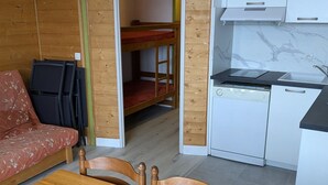 A compact kitchen with a dishwasher, a sink, and a microwave. There is a wooden table with chairs in the foreground. - Maxi studio 6 pers, central Orcières, near slopes (Orcières Merlette)