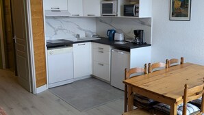 A compact kitchen with white cabinets, a black countertop, and a wooden dining table with chairs. - Maxi studio 6 pers, central Orcières, near slopes (Orcières Merlette)