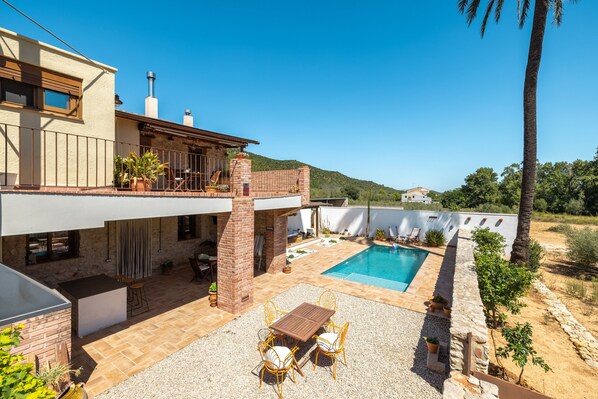 A modern house with a pool, outdoor seating, and a view of the hills.