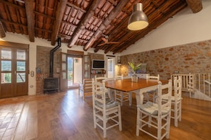 A dining area with a wooden table and white chairs, a fireplace, and a stone wall.