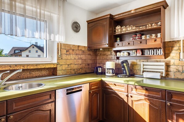 A kitchen with a sink, dishwasher, wooden cabinets, and a window with a view of a house.