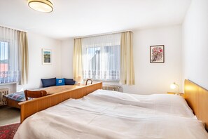 A hotel room with a large bed, a desk, a chair, a window with curtains, and a radiator. - Apartment 'Kropp' with Mountain View, Balcony, and Wi-Fi (Steinen)
