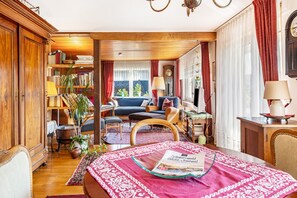 A cozy living room with a sofa, a coffee table with a magazine, a bookshelf, and a window with curtains.