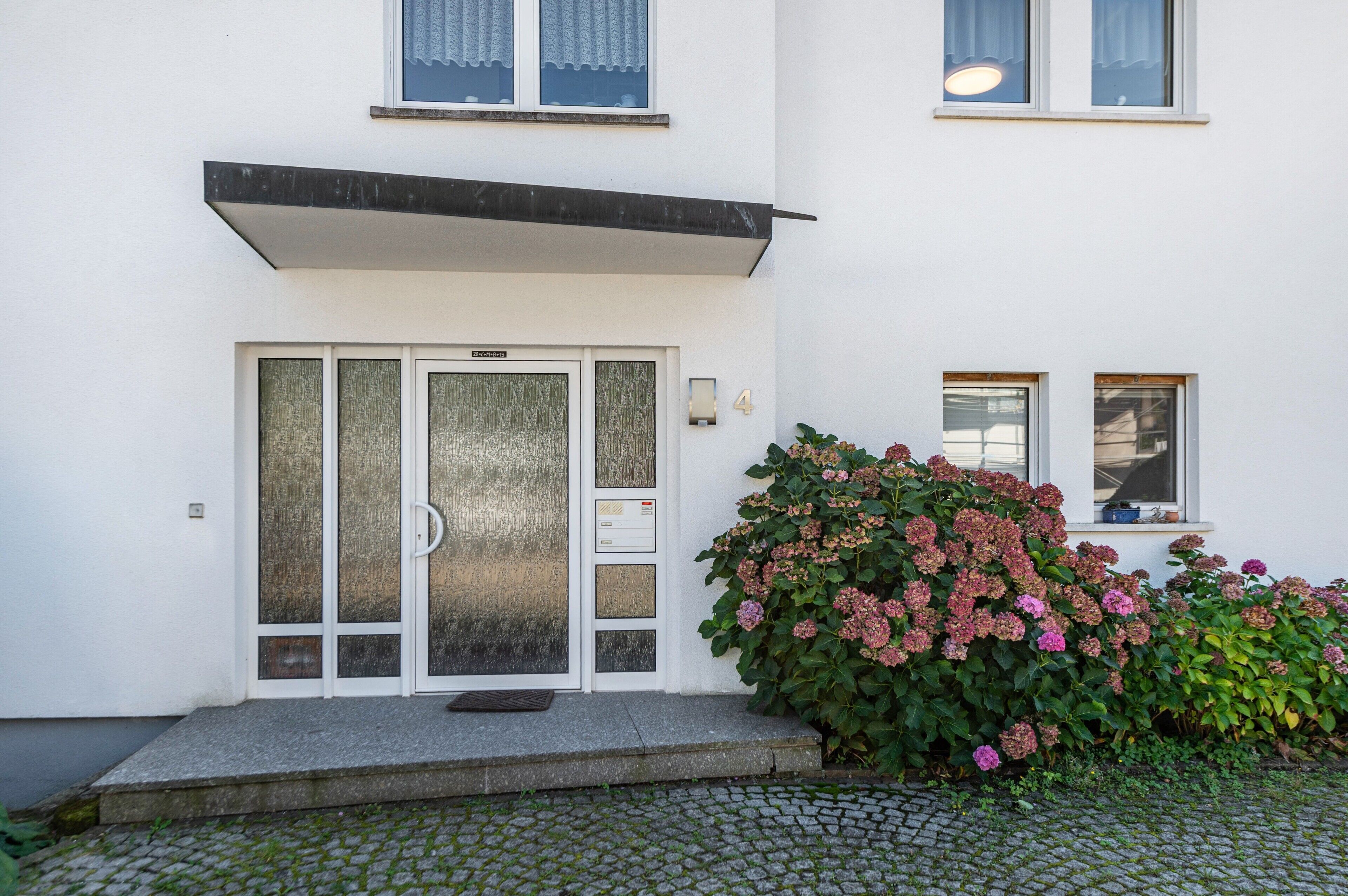 En byggnad med en vit fasad, en entré med en glasdörr och ett litet fönster med en lampa.
