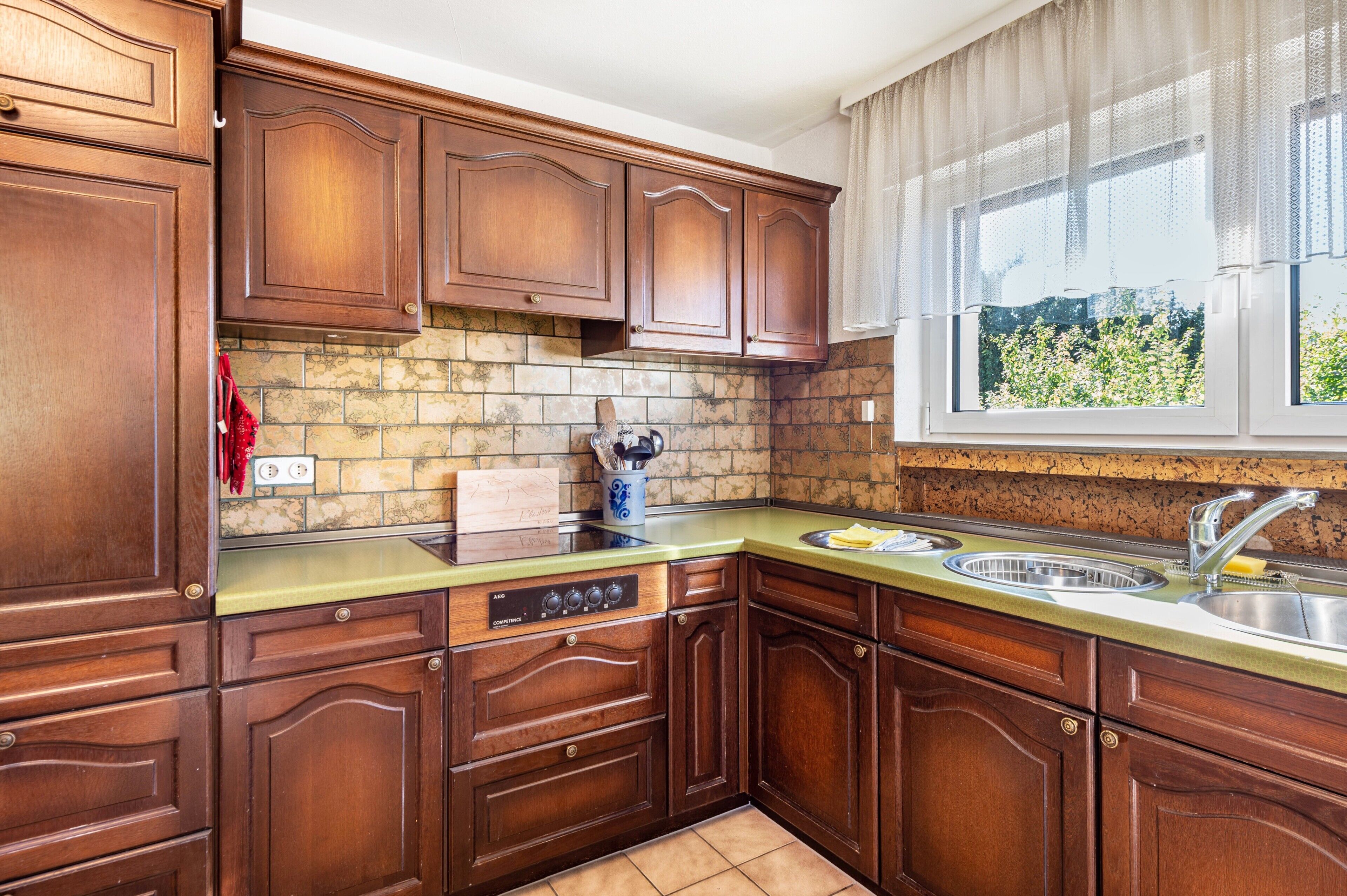 A kitchen with wooden cabinets, a built-in oven, a double sink, and a window with a view of greenery.