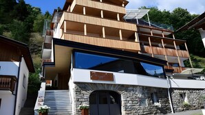 A multi-story building with a stone facade, wooden balconies, and a large glass window. - Apartment 'Gipfelglück 1' with Mountain View, Shared Terrace and Wi-Fi (Malles Venosta)