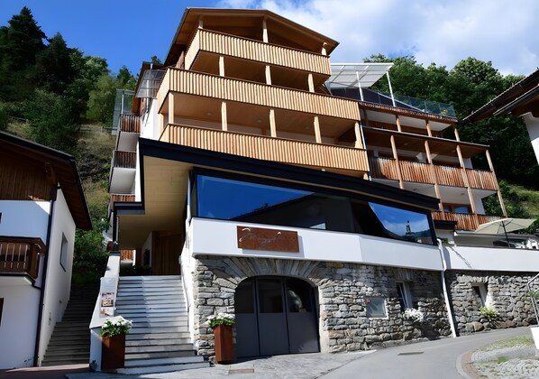 A multi-story building with a stone facade, wooden balconies, and a large glass window.