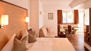 A hotel room with a large bed, bedside lamps, a sofa, a dining table, and a view of the outdoors. - Apartment 'Gipfelglück 1' with Mountain View, Shared Terrace and Wi-Fi (Malles Venosta)