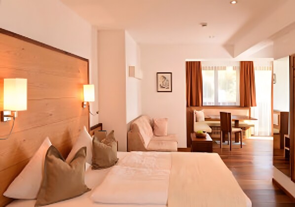 Habitación de hotel con una cama grande, lámparas de noche, un sofá, una mesa de comedor y vistas al exterior.
