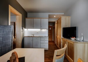 A modern kitchen with a built-in oven, a dining area with a table and chairs, and a TV on a wooden cabinet.