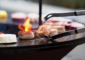 A grill with sausages and a white item, possibly cheese, being cooked over an open flame.