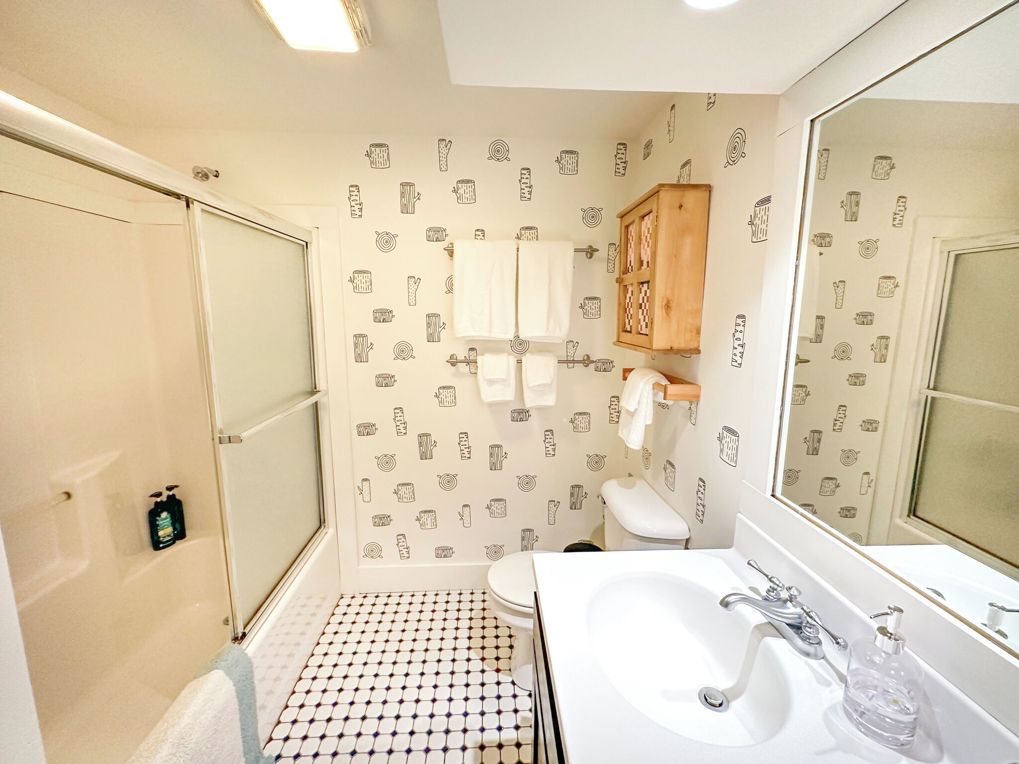 Ein Badezimmer mit gefliestem Boden, einem weißen Waschbecken, einem Spiegel und einem Holzkabinent.