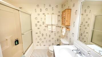 Ein Badezimmer mit gefliestem Boden, einem weißen Waschbecken, einem Spiegel und einem Holzkabinent.
