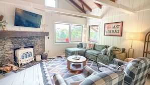 A cozy living room with a stone fireplace, a large flat-screen TV, and a 'This must be the place' sign.