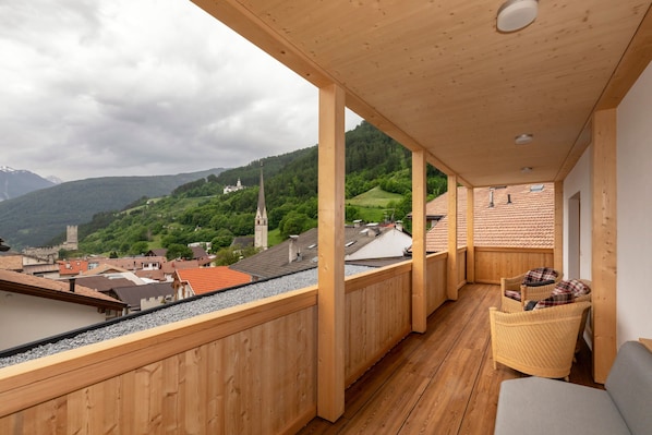 Un balcon en bois offrant une vue sur un village, le clocher d’une église et une montagne.