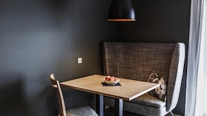 Un petit coin repas avec une table, un saladier de fruits, une chaise et une suspension noire.