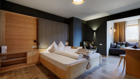 Une chambre d’hôtel moderne avec un lit en bois, un canapé gris, un bureau et une lampe fixée au mur.
