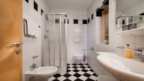 Une salle de bain avec douche, toilettes, bidet, lavabo et un carrelage à motifs carrés.