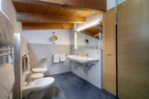 Une salle de bain moderne équipée de toilettes, d’un bidet et d’un lavabo, avec des poutres en bois au plafond et un miroir.