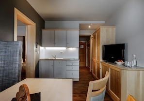 A modern kitchen with a built-in oven, a dining area with a table and chairs, and a TV on a wooden cabinet.