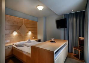 A bedroom with a wooden headboard, a bed, a bedside table, a TV mounted on the wall, and a chair.
