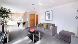 A modern living room with a sofa, a coffee table, and a kitchen in the background. - Spacious 3 Bed in Aberdeen s Westend (Aberdeen)
