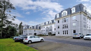 A multi-story building with a grey facade and large windows. There are several cars parked in front, and a well-maintained lawn area. - Spacious 3 Bed in Aberdeen s Westend (Aberdeen)