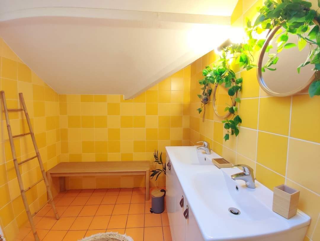 A bathroom with yellow tiles, a bench, a sink, and a potted plant.