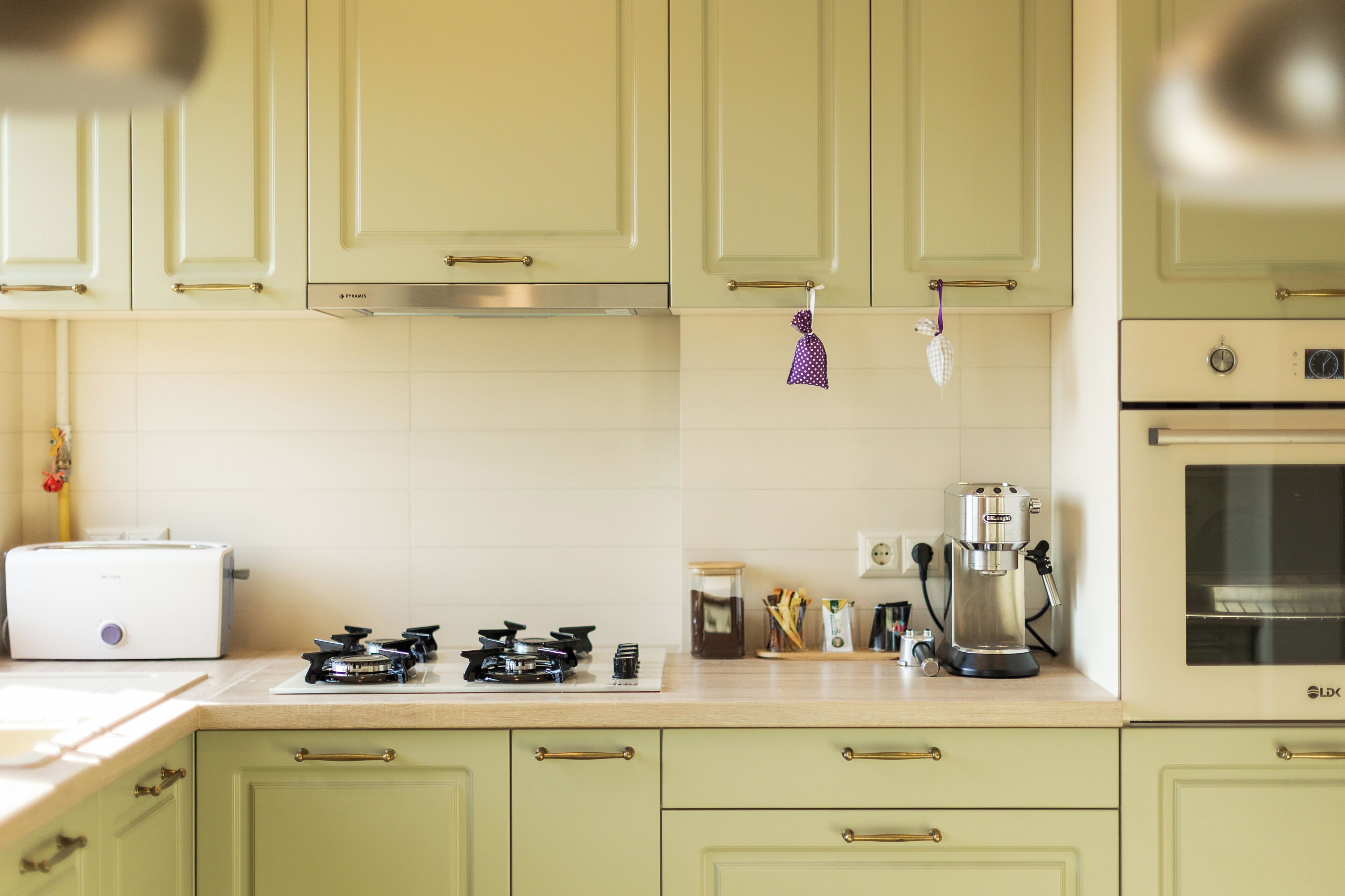 Une cuisine avec des meubles de couleur vert clair, une cuisinière à gaz, une machine à café et un grille-pain.