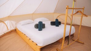 A tent with a bed, pillows, and a wooden hanger rack.