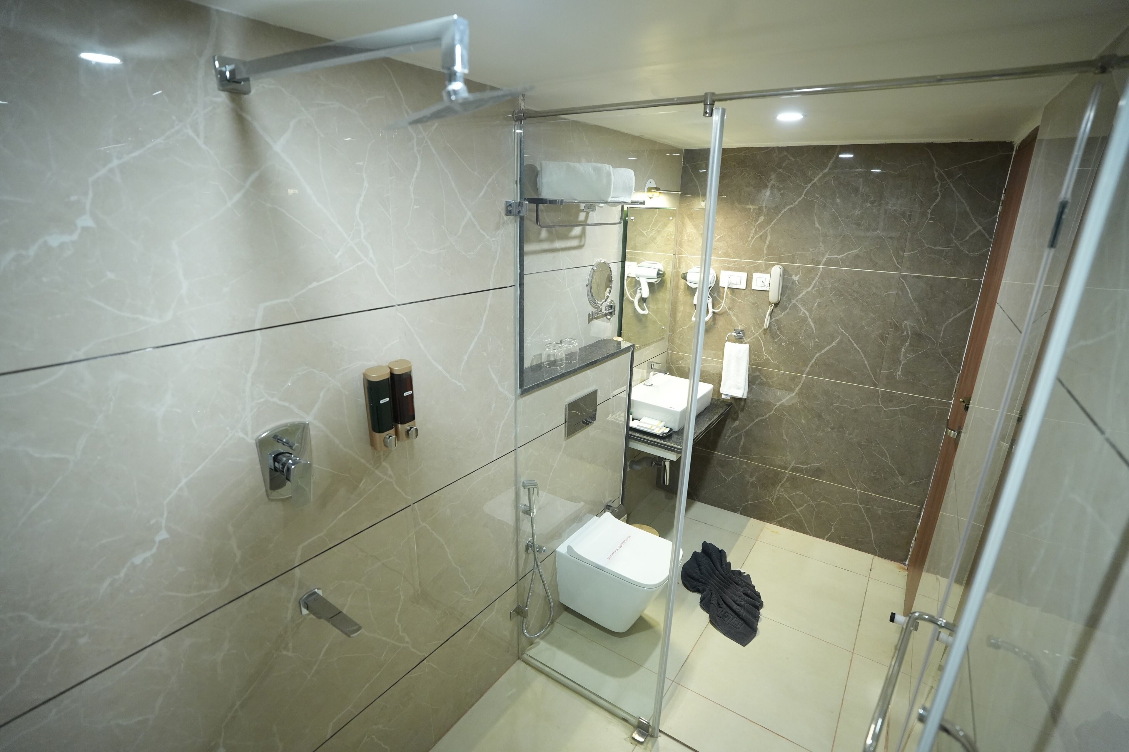 A modern bathroom with a glass-enclosed shower, marble walls, and a glass shower door.