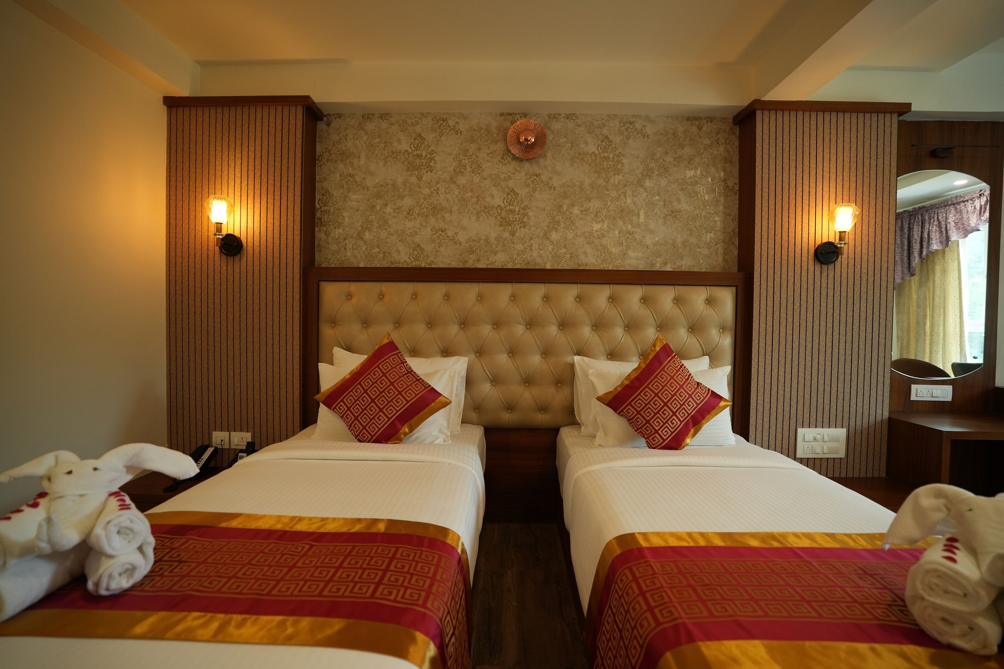 A hotel room with two beds, a tufted headboard, wall sconces, and a mirror.