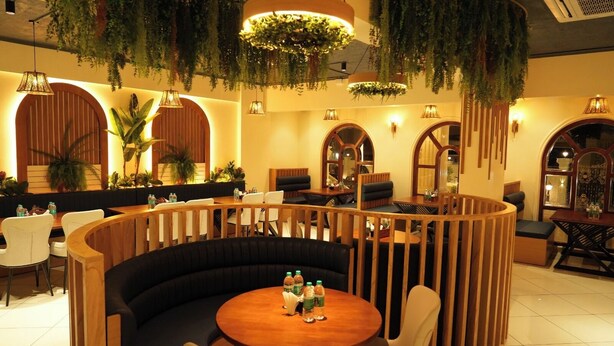 Un restaurante con área de mesas tipo cabina de madera, plantas colgantes e iluminación cálida.