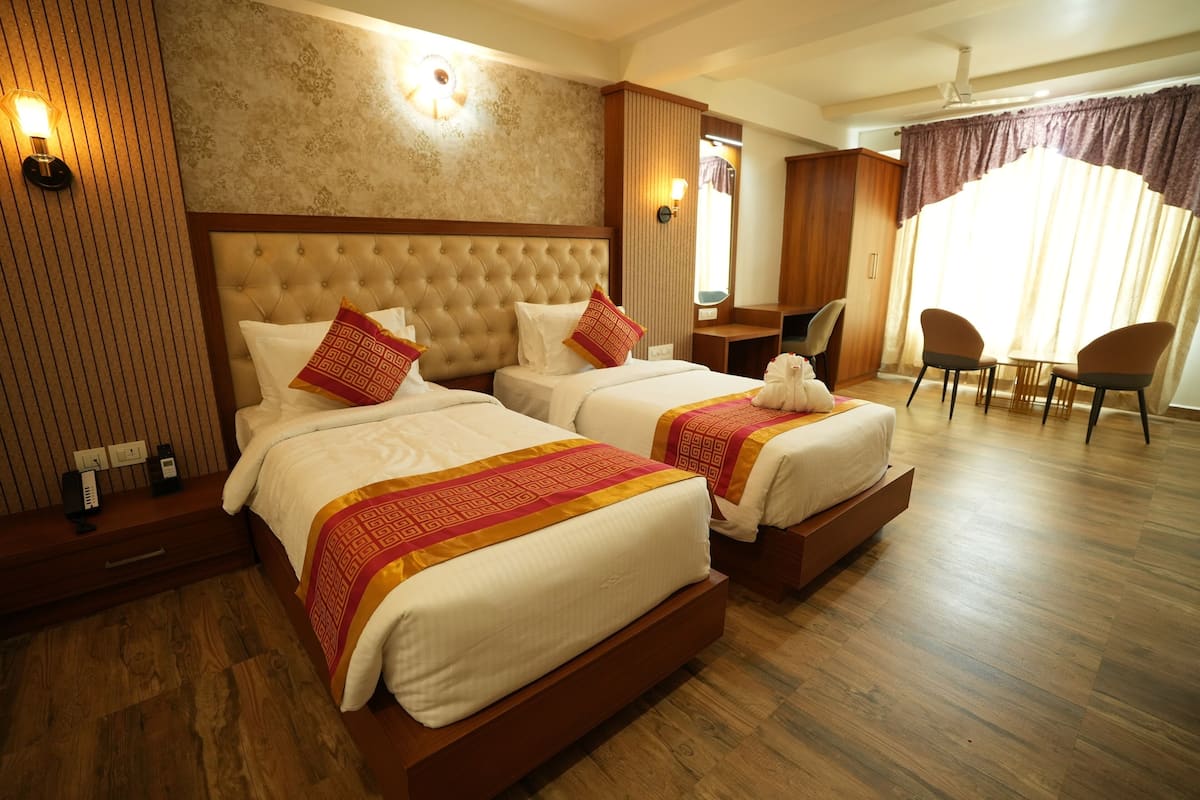 Ein Hotelzimmer mit zwei Betten, einem Schreibtisch, einem Stuhl und einem großen Fenster mit Vorhängen.