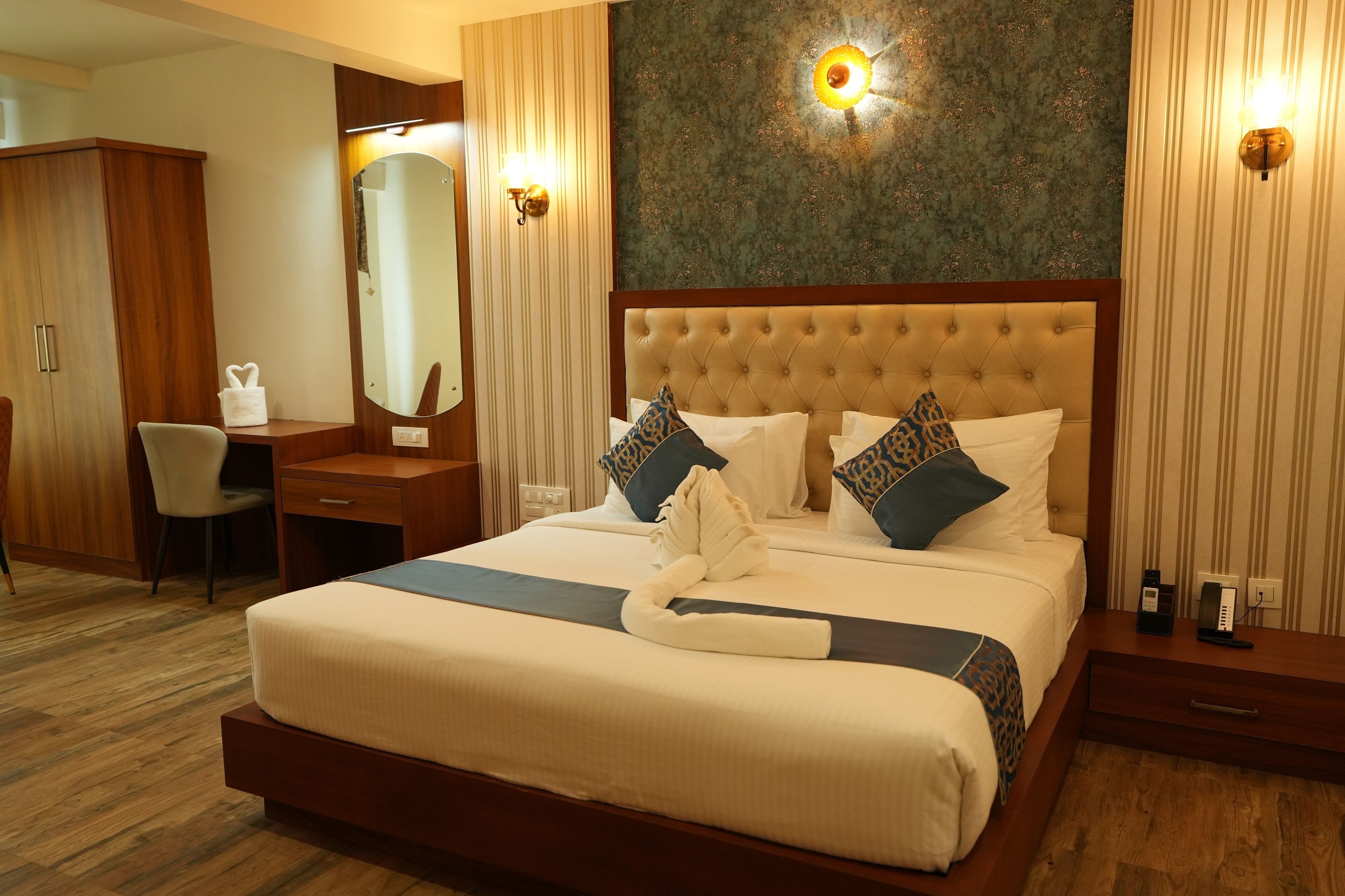 A hotel room with a large bed, a desk, a chair, a wardrobe, and a mirror.