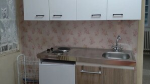 A compact kitchen with white cabinets, a sink, a small refrigerator, and a metal rack.
