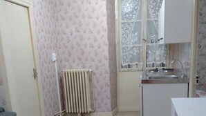 A small, compact room with a radiator, a sink, and a window with lace curtains.