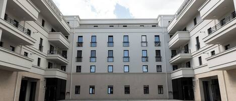 A modern multi-story building with a central courtyard, balconies, and a flat roof.