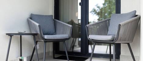 A modern outdoor seating area with two chairs and a small table, positioned near a glass door leading to an outdoor space.